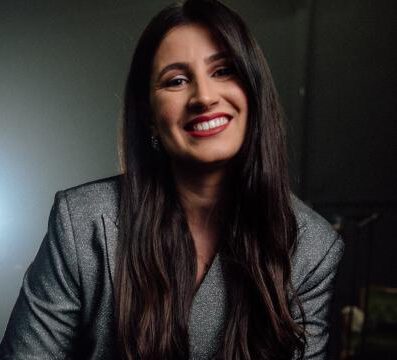 Svenia Ribeiro, Gesangscoach, lächelt in die Kamera vor dunklem Hintergrund